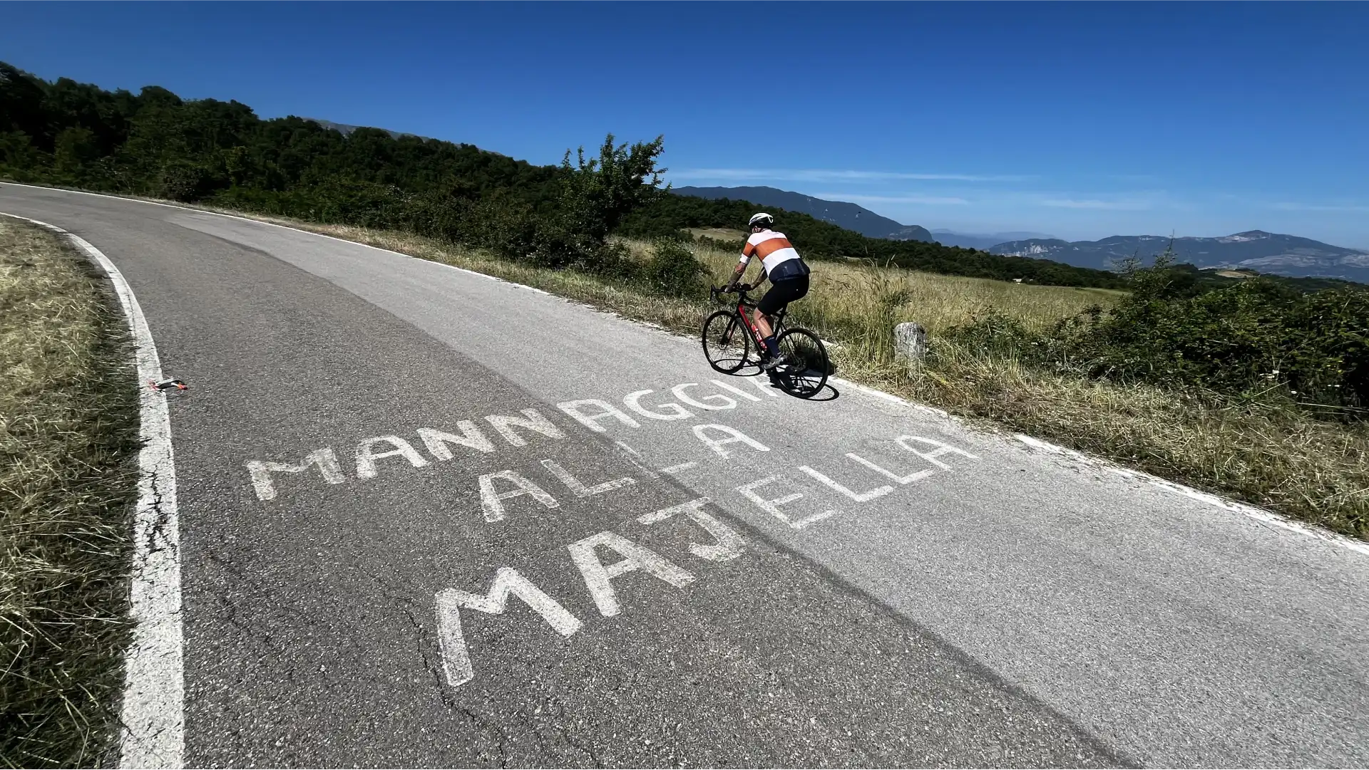 Cyclist climbing Blockhaus in Abruzzo with writing on the road ‘Mannaggia alla Majella’