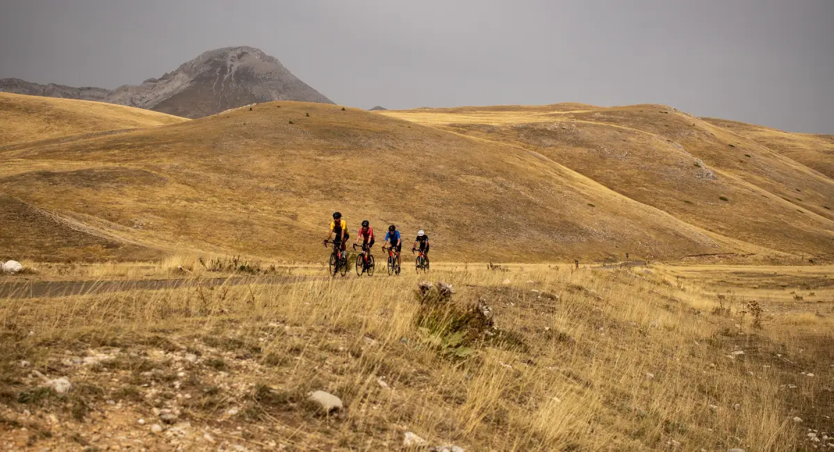 Group of cyclists riding across the high plains of Campo Imperatore under the Gran Sasso