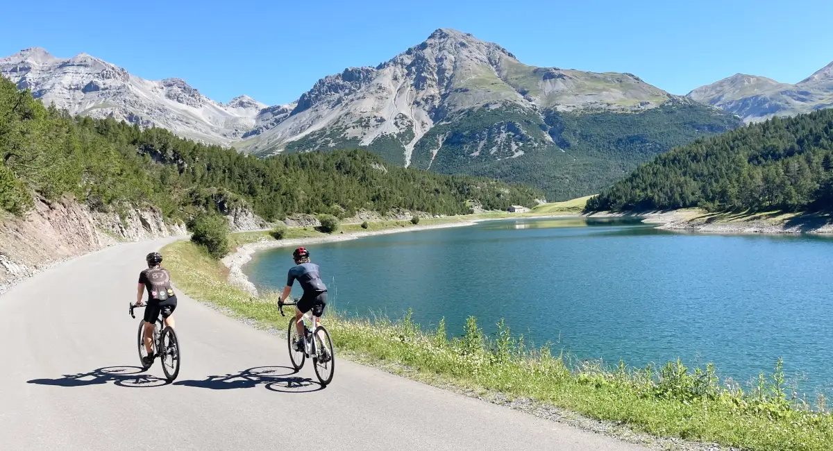 Cyclists riding along the turquoise Cancano Lakes surrounded by alpine peaks on the Stelvio and Dolomites Bike Tour