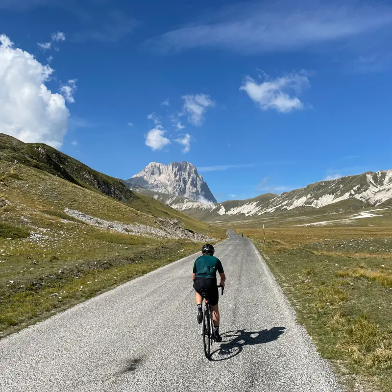 Road cyclist heading towards Campo Imperatore with Corno Grande peak in the background, Abruzzo