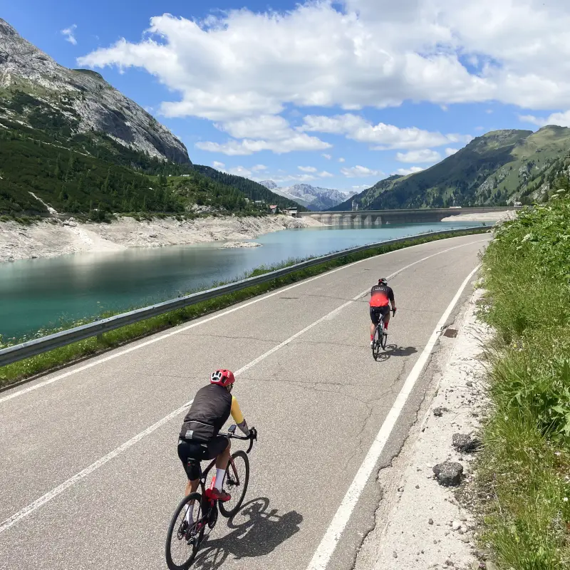 Cyclists riding along Lake Fedaia with the Marmolada in the background