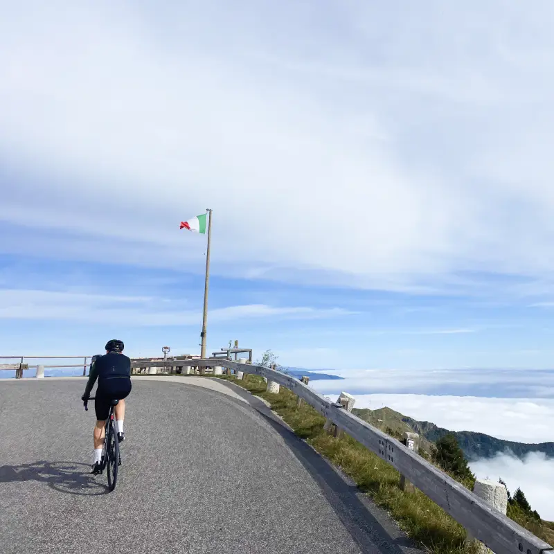 Cyclist reaching the summit of Monte Grappa with the Italian flag in view
