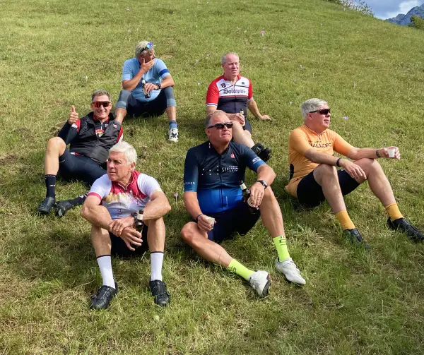 Group of cyclists relaxing on a grassy slope after a big mountain ride during the Stelvio and Dolomites Bike Tour