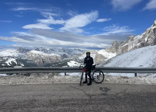 Cyclist standing with bike on a snowy Sella Ronda route surrounded by the Dolomites peaks