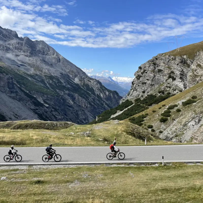 Three cyclists climbing the Stelvio Pass on a sunny day during the E-bike the Alps tour