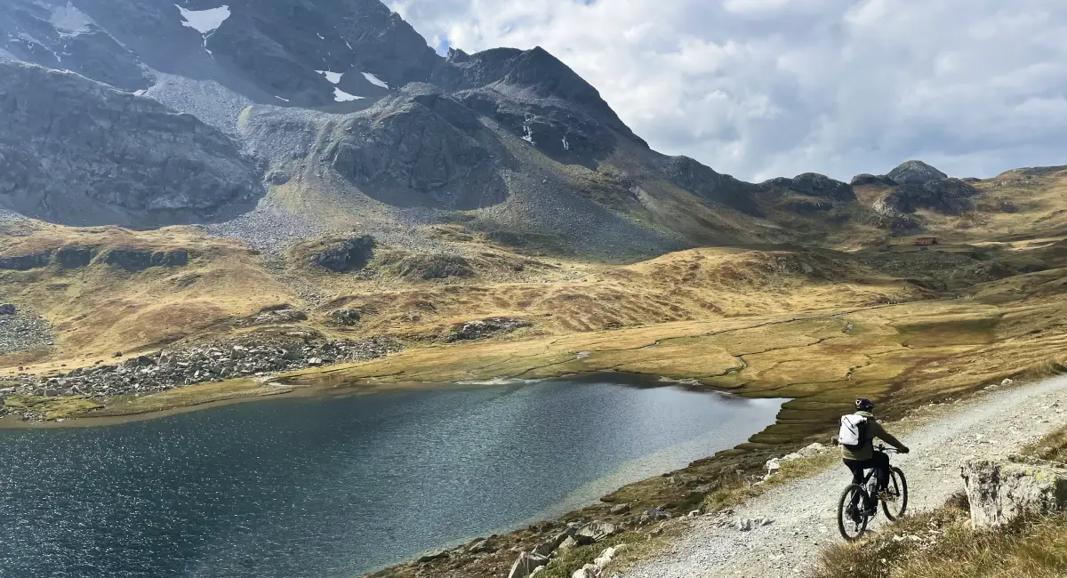 Cyclist riding along a mountain lake in Val Viola, surrounded by untouched alpine landscapes
