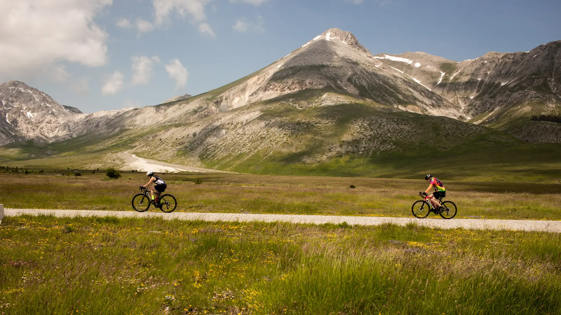 Cyclists riding across Campo Imperatore plateau beneath the Gran Sasso mountains during the Wild Abruzzo Road Bike Tour