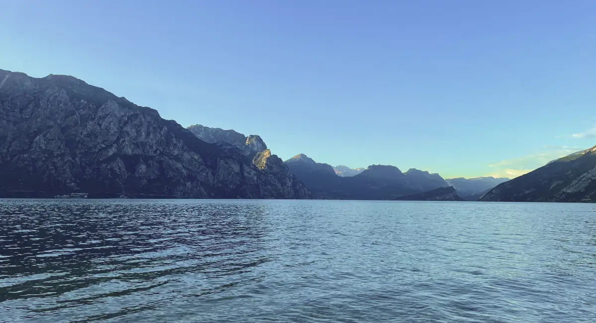 Peaceful evening view of Lake Garda surrounded by dramatic limestone cliffs and blue mountain silhouettes