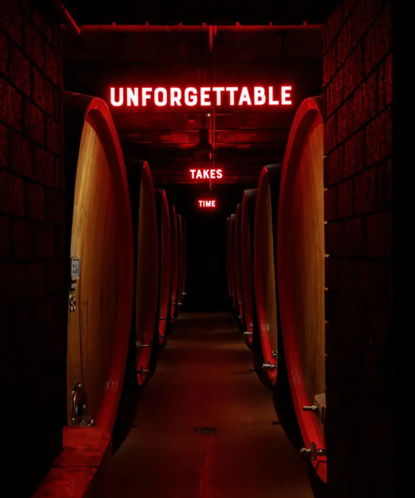 Rows of oak barrels in the Braulio cellar with red neon lights reading unforgettable takes time