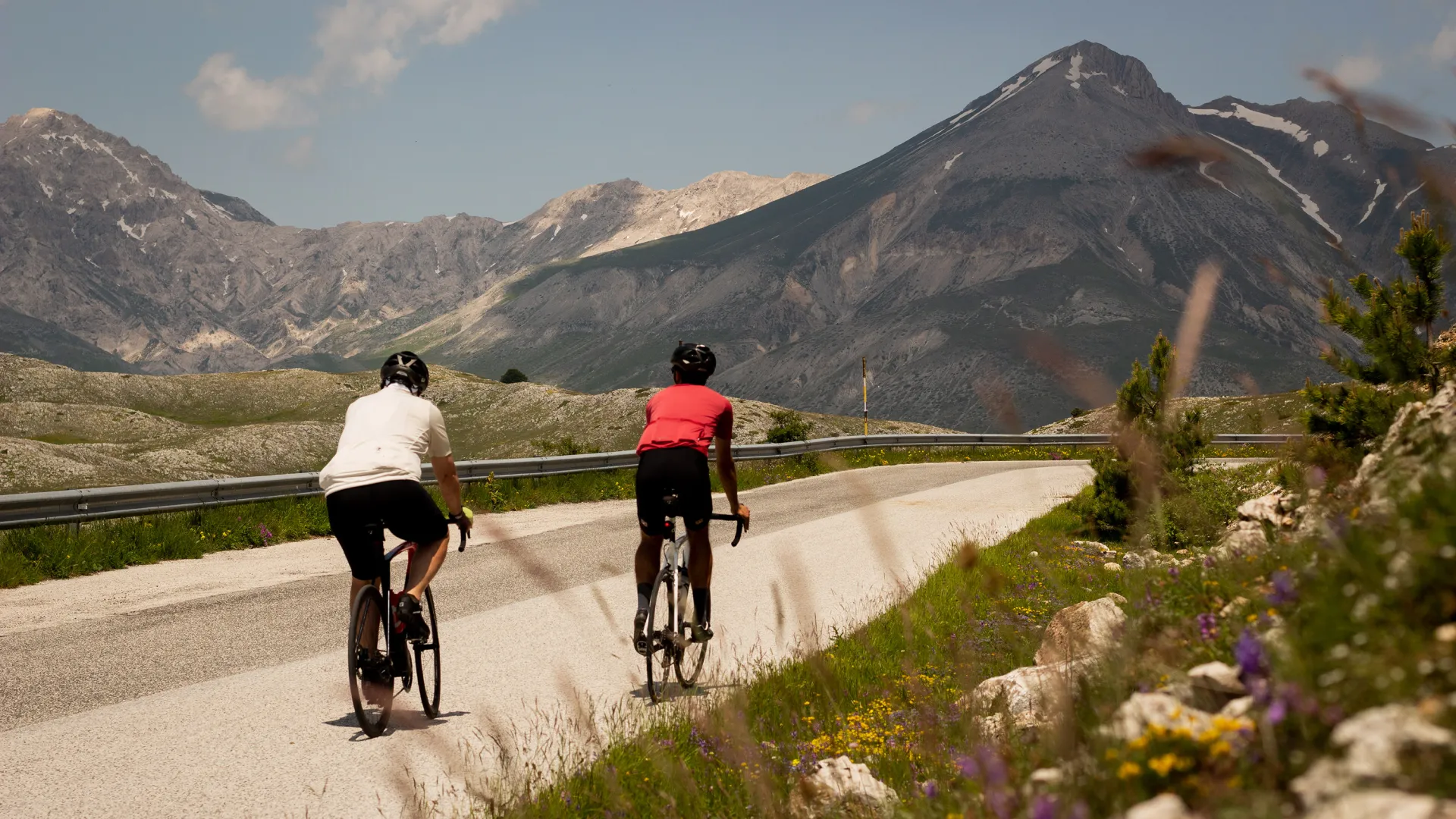 Two cyclists riding towards the Gran Sasso mountains on the scenic road to Campo Imperatore in Abruzzo, Italy