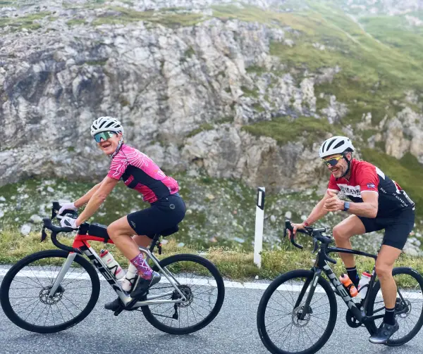 Smiling couple climbing the Stelvio Pass pass on their road bikes during a Vago Cycling tour in Italy
