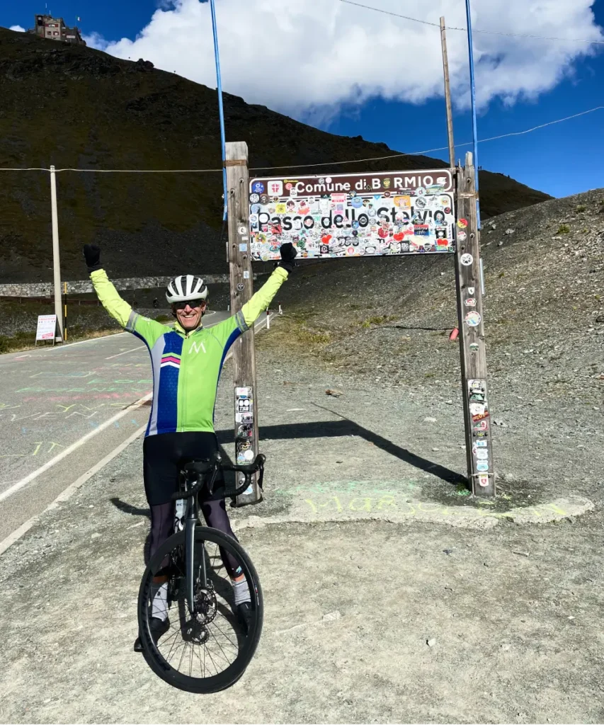 Cyclist celebrating at the Passo dello Stelvio summit sign after a challenging climb