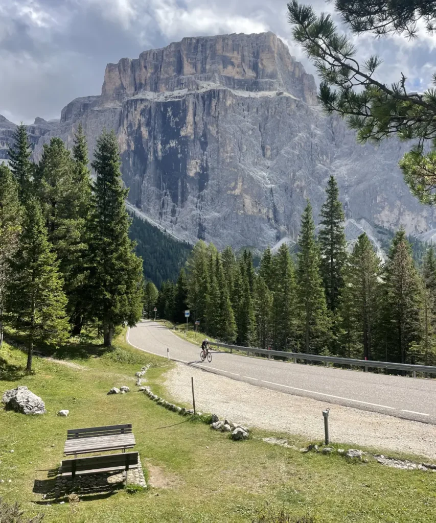 Cyclist riding through pine forests beneath the towering cliffs of Passo Sella in the Dolomites