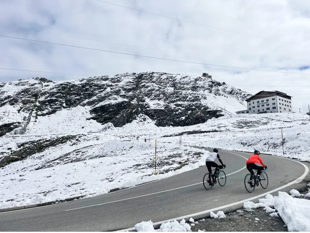 Two cyclists riding through snow-covered roads near the summit of the Stelvio Pass