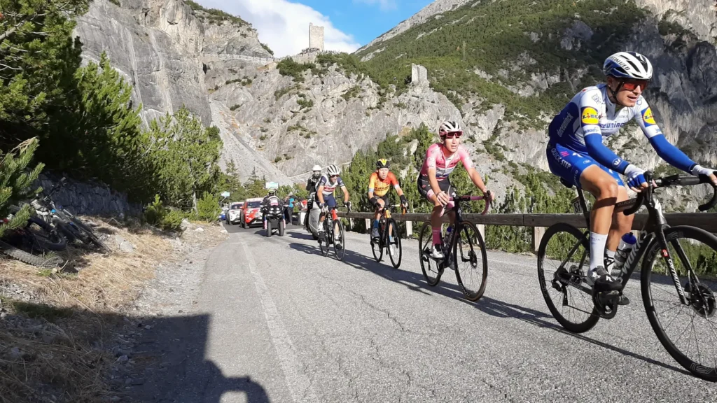 Giro d’Italia riders climbing the road to Cancano surrounded by rocky cliffs and support cars