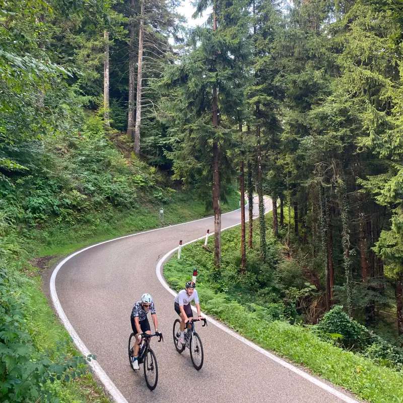 Cyclists climbing the Monte Velo ascent through forested switchbacks near Lake Garda