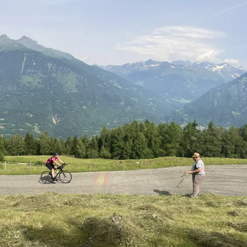 Cyclist climbing Passo Mortirolo in Valtellina with a local farmer in the background and mountain views all around