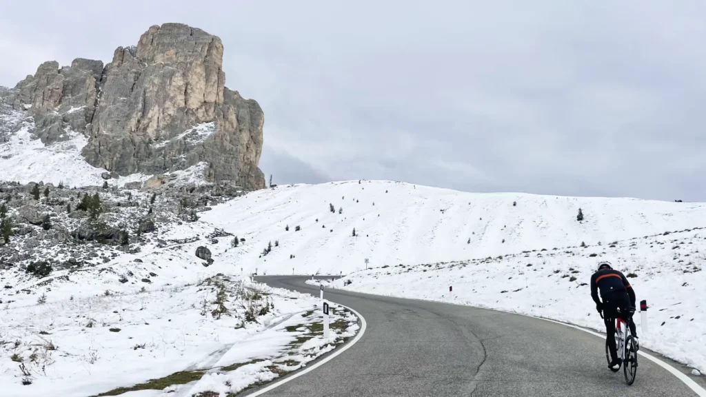 Cyclist climbing the snow-covered road to Passo Giau in the Dolomites under a cloudy sky