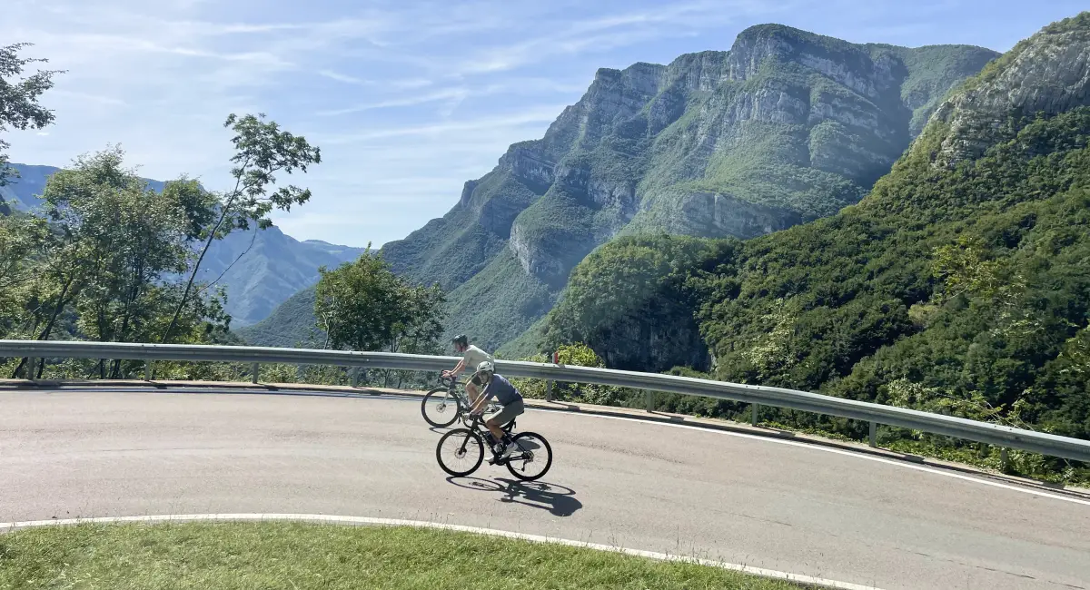 Cyclists tackling a mountain hairpin on Passo San Valentino with panoramic views over the Brenta Dolomites
