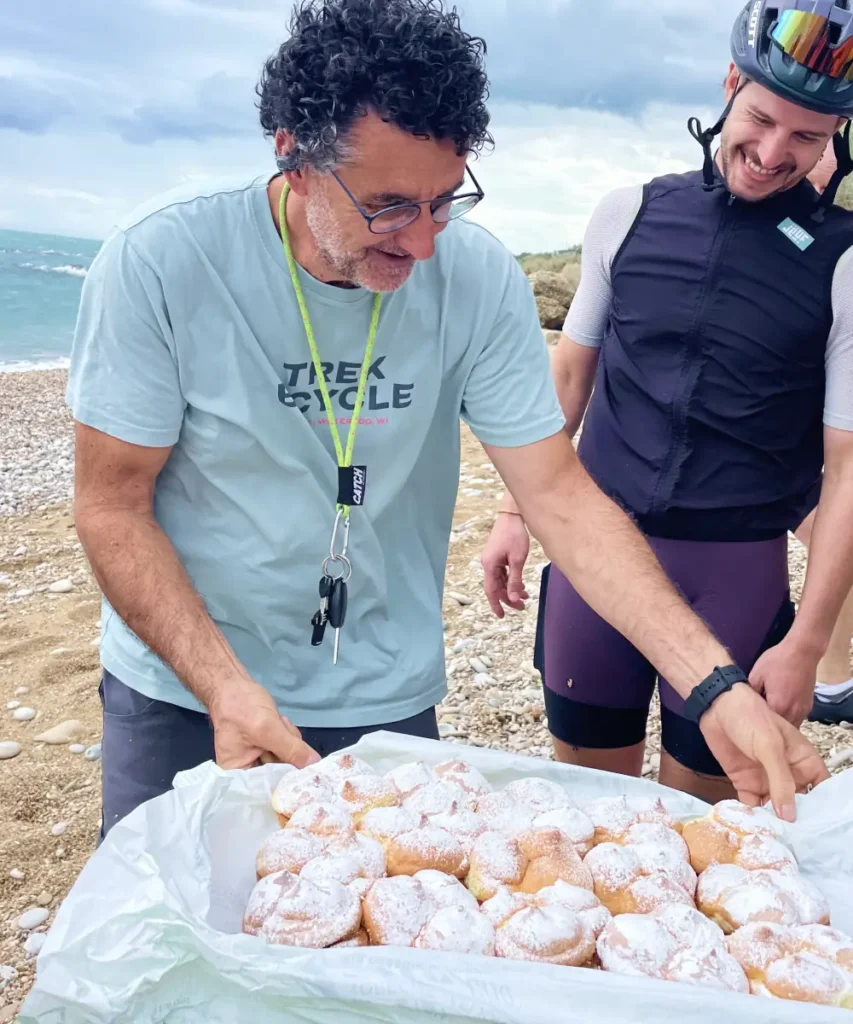 Vago Cycling team serving Sise delle Monache pastries during a seaside picnic in Abruzzo