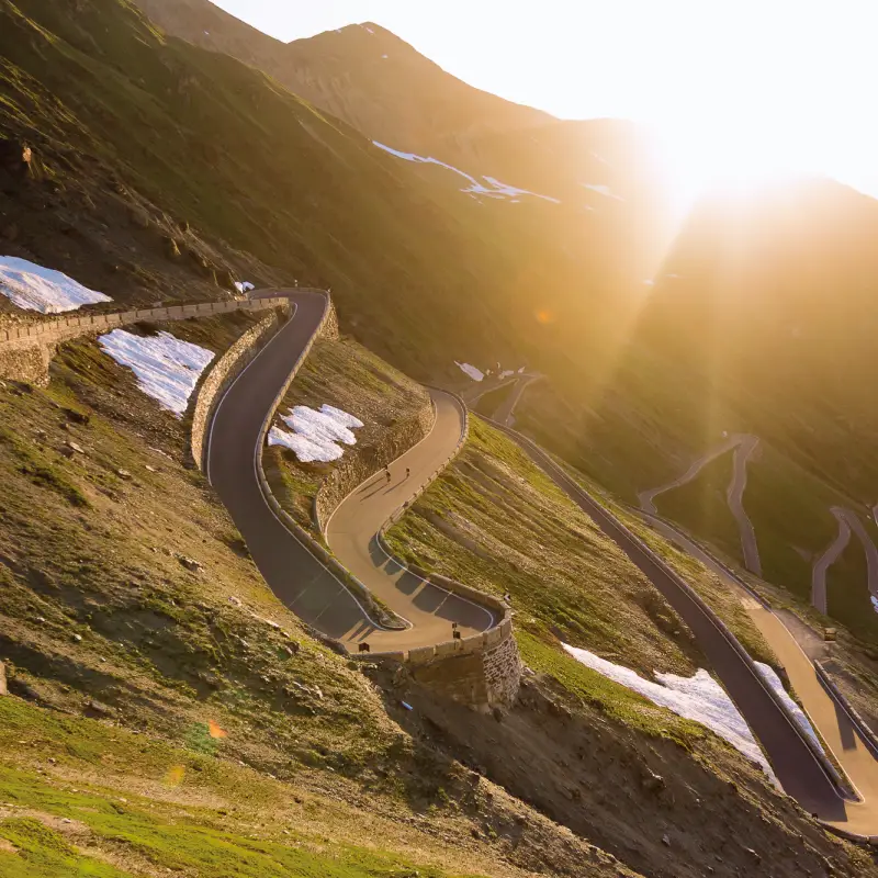 Golden sunrise illuminating the switchbacks of Stelvio Pass with cyclists climbing through the alpine landscape