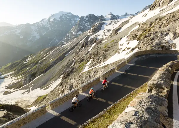 Cyclists riding at sunrise on the upper slopes of Stelvio Pass surrounded by snow and dramatic alpine peaks