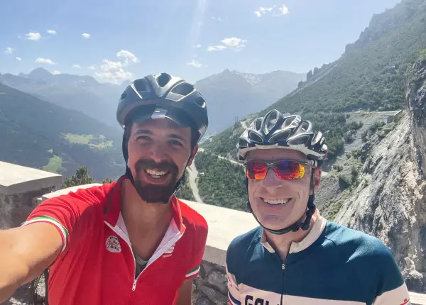 Vago Cycling guide smiling with a guest on a scenic mountain road in Italy, representing the friendly Vago Way